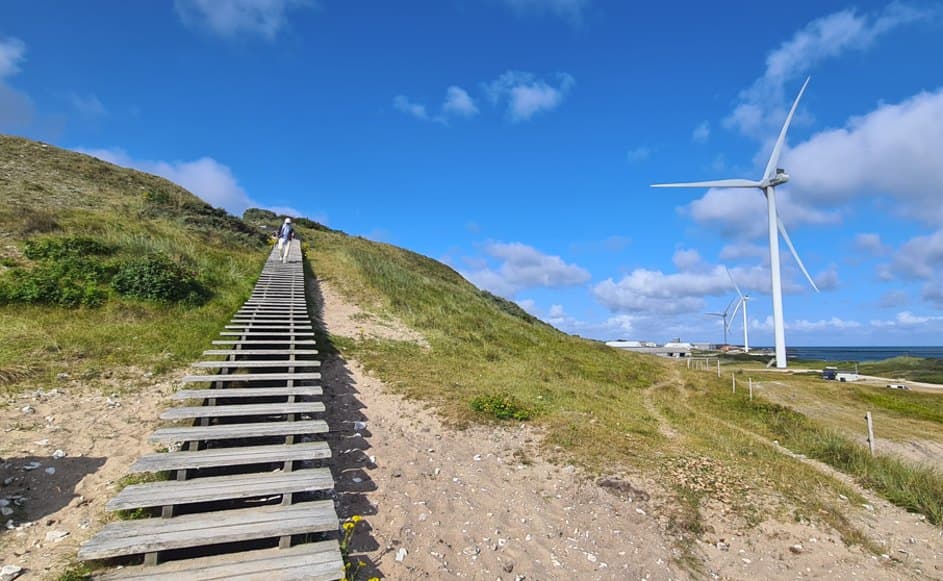 Wooden steps up a dune towards wind turbines by the sea